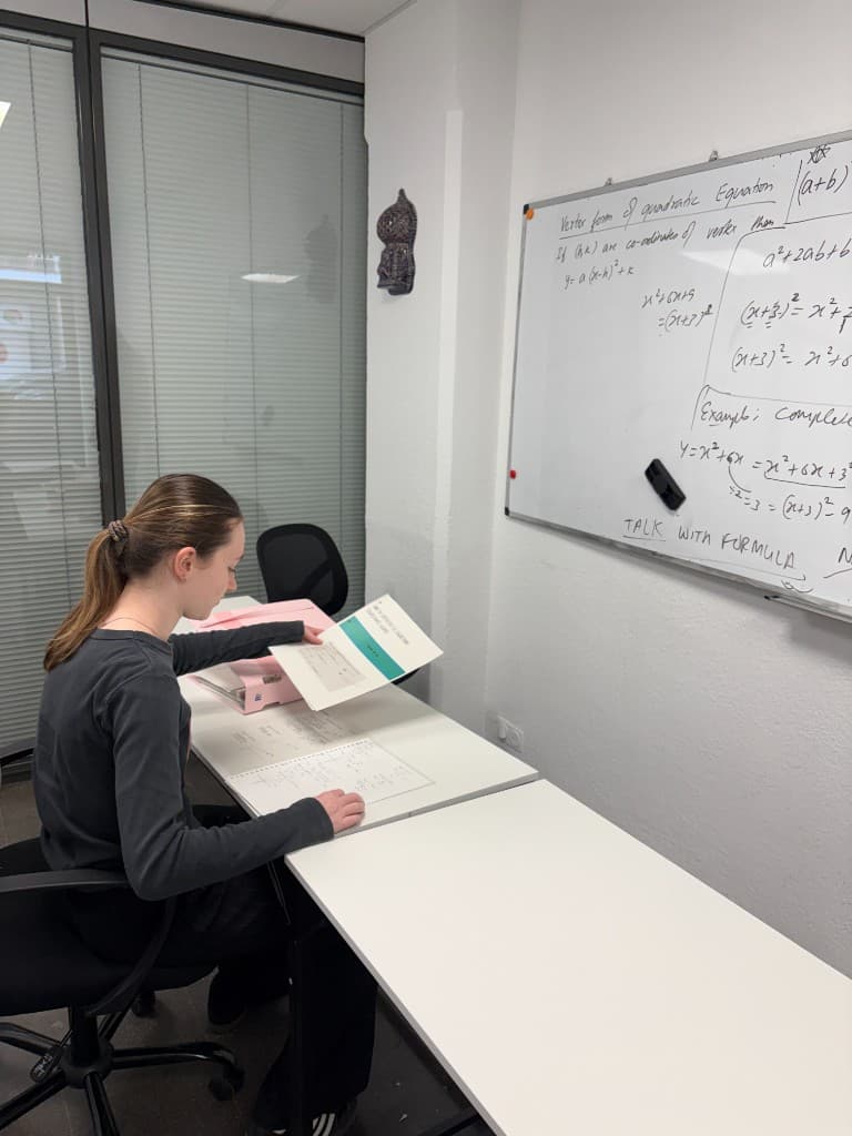 Student working through mathematics exercises beside a whiteboard.