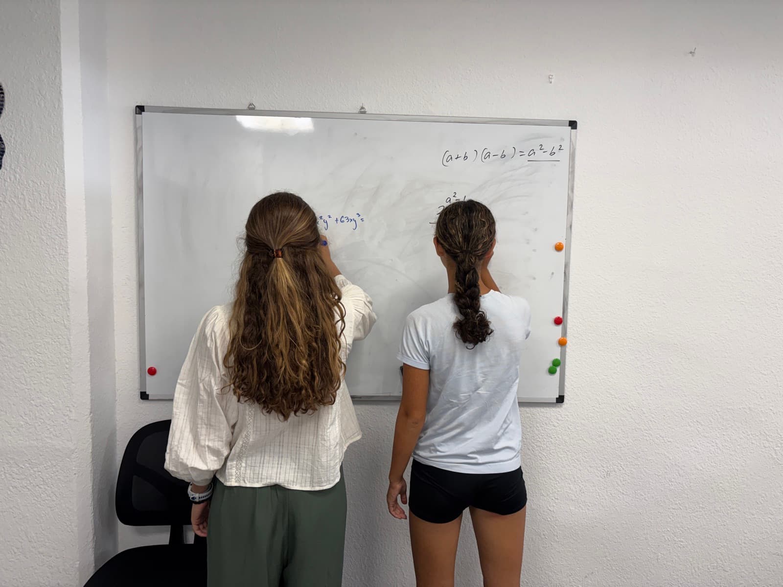 Two students solving maths problems together at the whiteboard.
